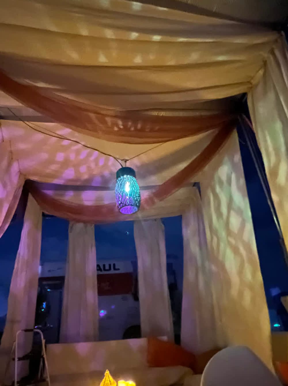 The finished lantern hanging and lit in the camp lounge at night, throwing patterns across the muslin