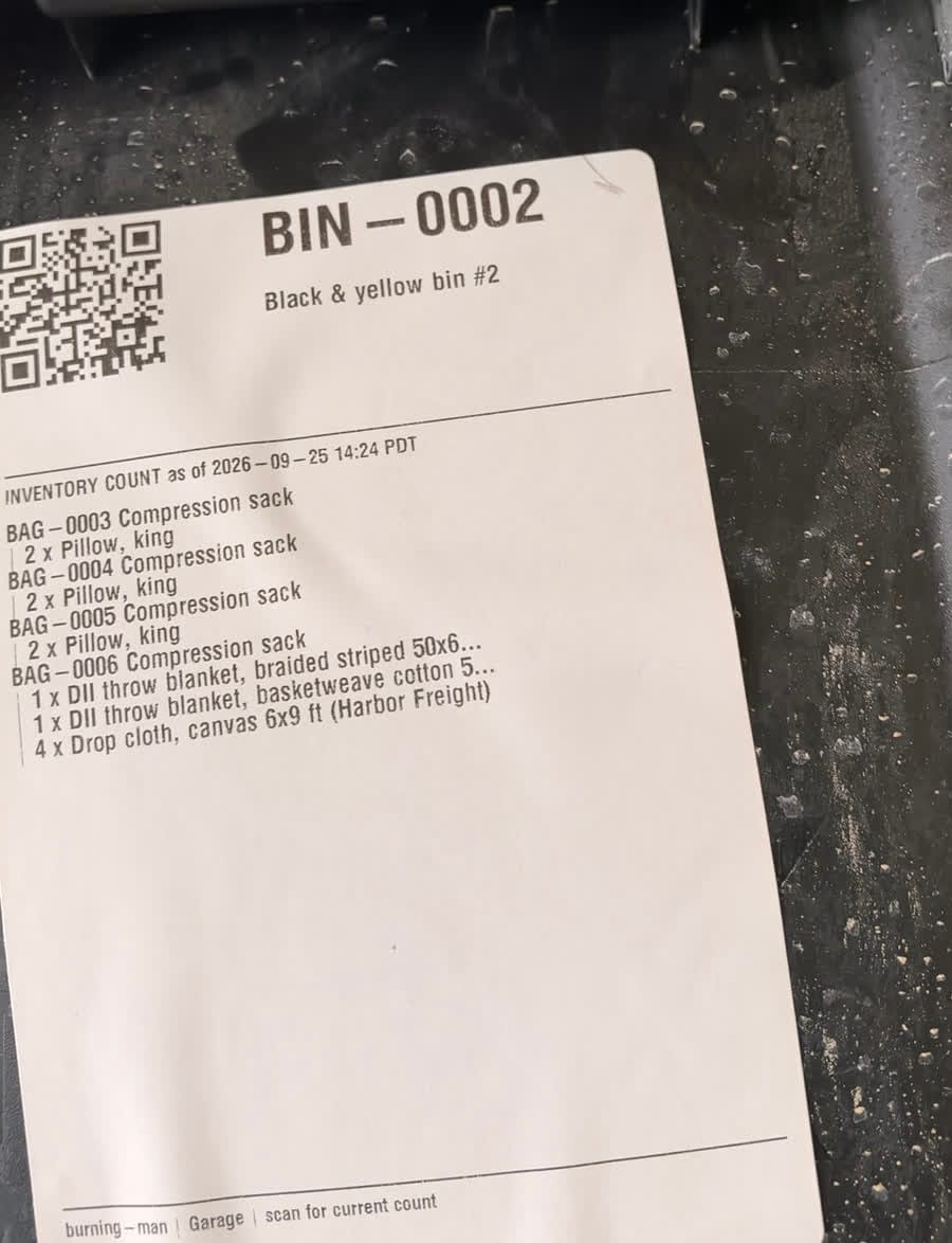 A printed label on a storage bin reading BIN-0002 with a QR code and an inventory count of what's inside